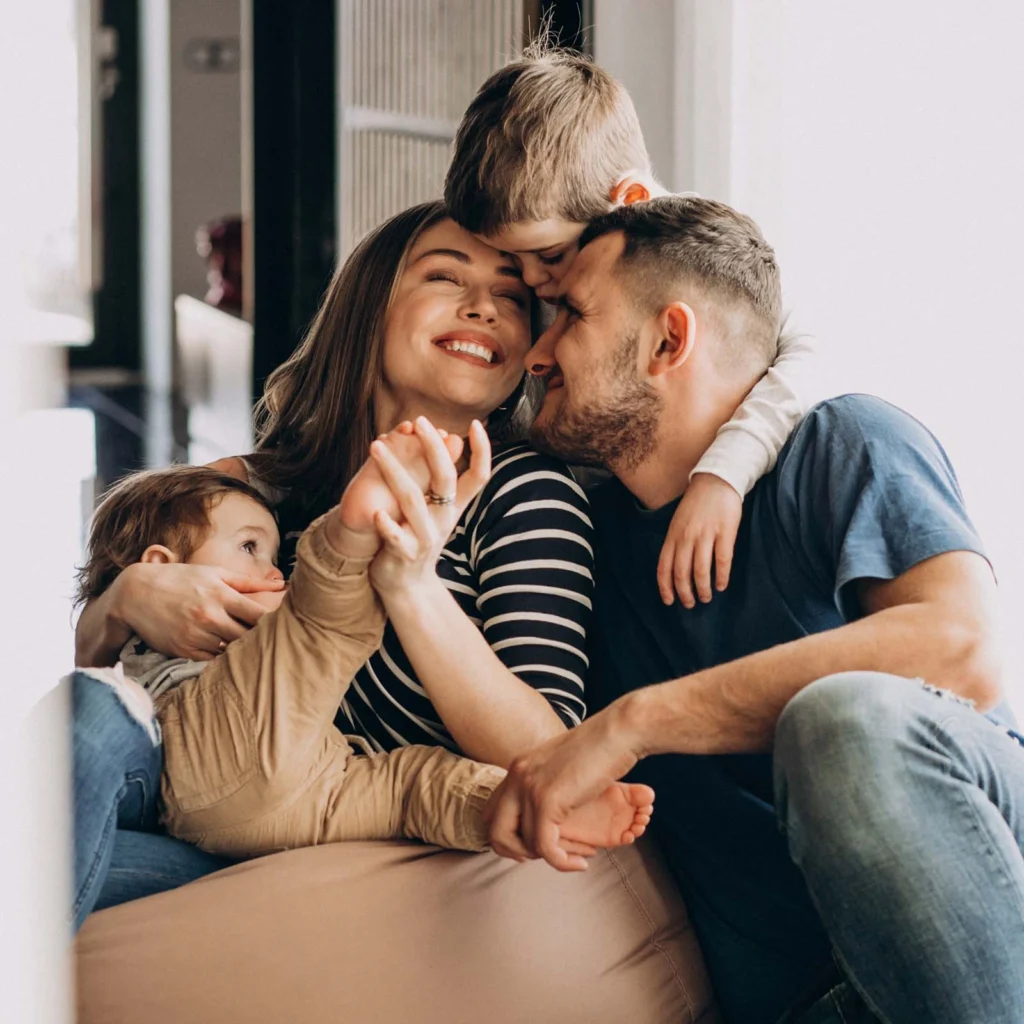 Fröhliche Familie sitzt eng umarmt auf einem Sofa und lacht.